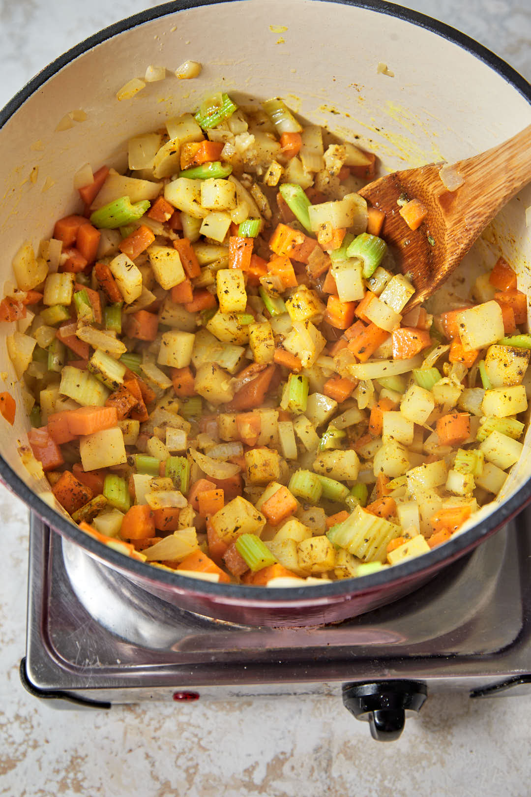 sautéed vegetables stirred with garlic and dried spices in a red pot.