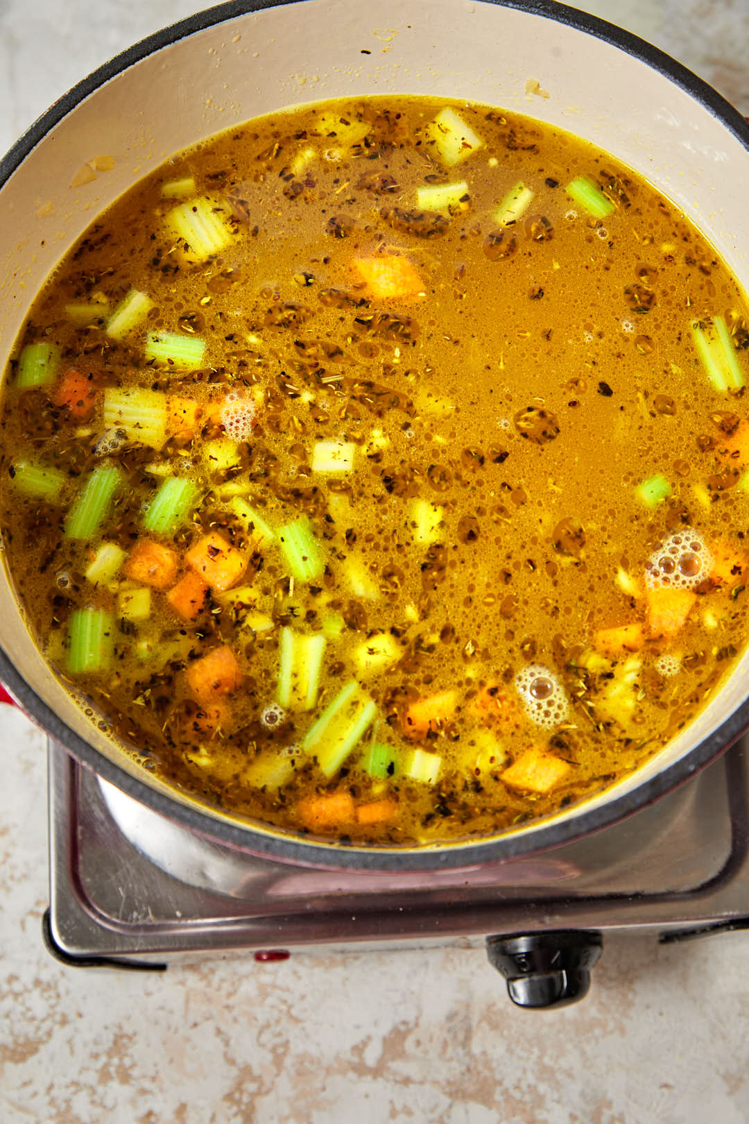 water added to the spiced vegetables in a red pot.