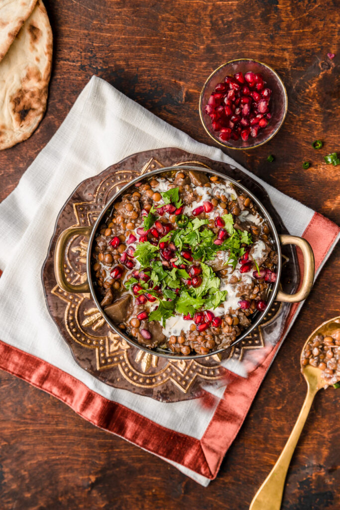 lentil pomegranate stew in bowl with a spoon and pomegranate seeds on the side