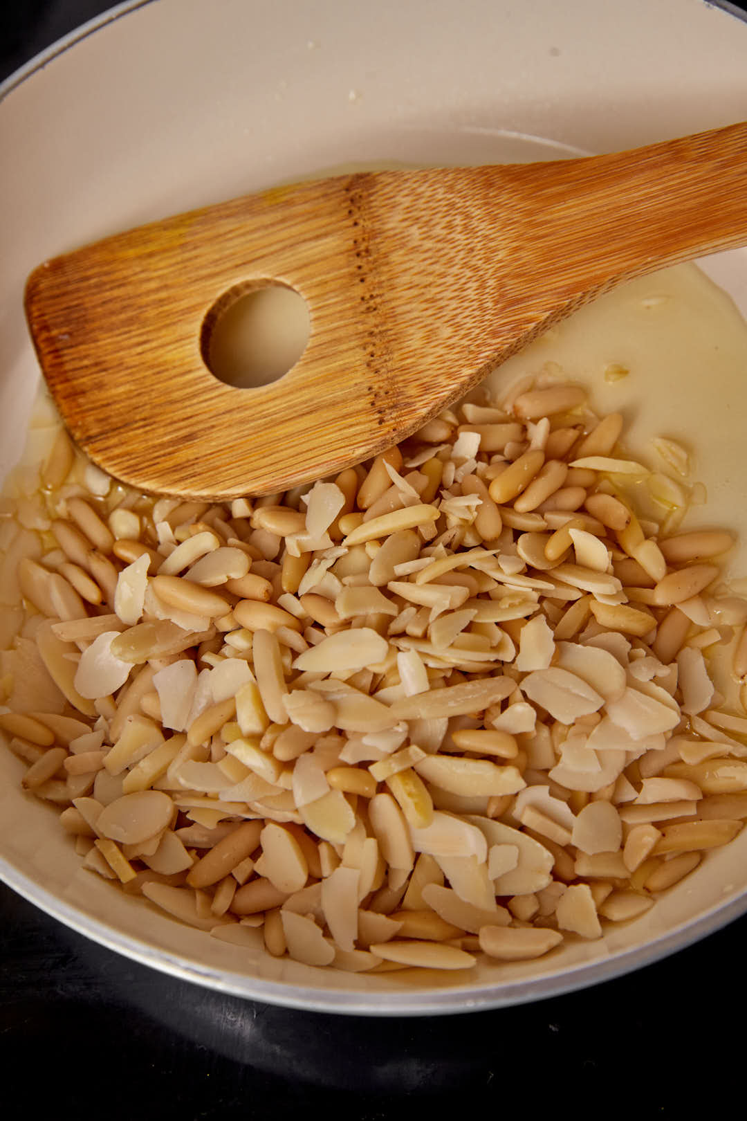 nut slivers in hot ghee being toasted in a skillet with a wooden spoon.