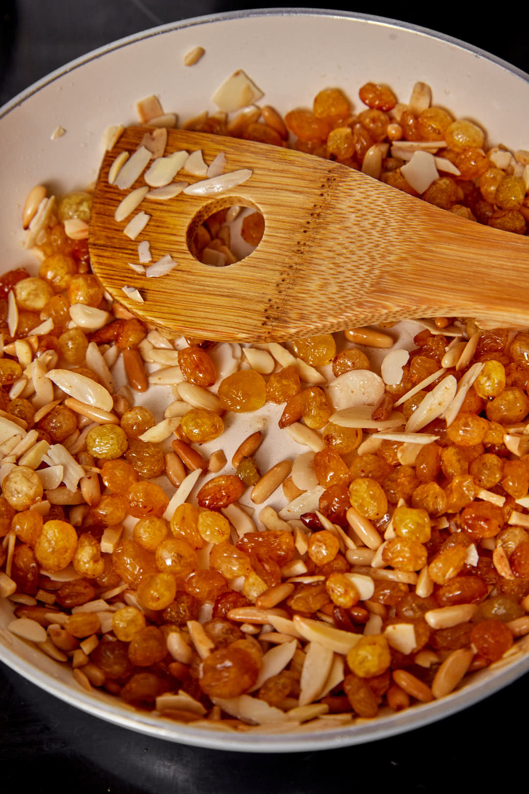 toasted nuts and raisins in a hot skillet with a wooden spoon.