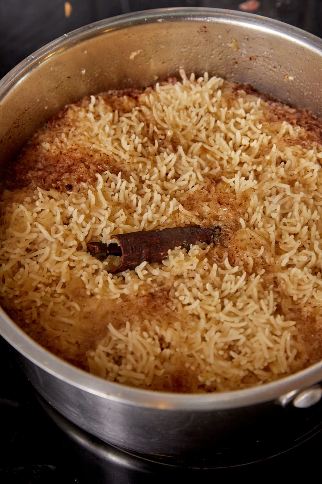 cooked egyptian rice in a large saucepan with a cinnamon stick.