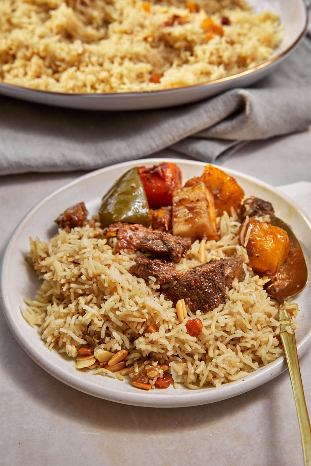 Rice and raisin pilaf on a white plate with beef and vegetable stew on the side.