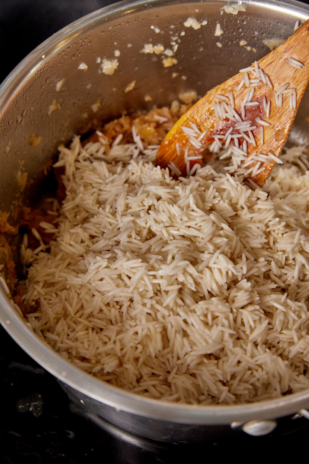 Basmati rice before cooking added to a large pot with a wooden spoon in it.