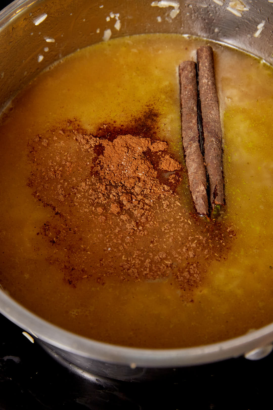 Cinnamon powder, broth, and a cinnamon stick added to a large pot of rice.