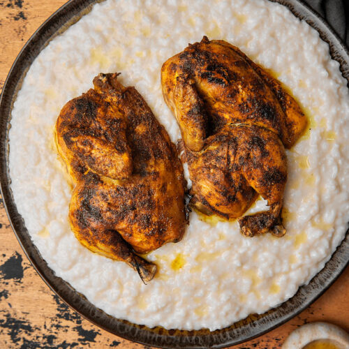 a platter of saleeg with roasted chicken halves on it on a wooden background.