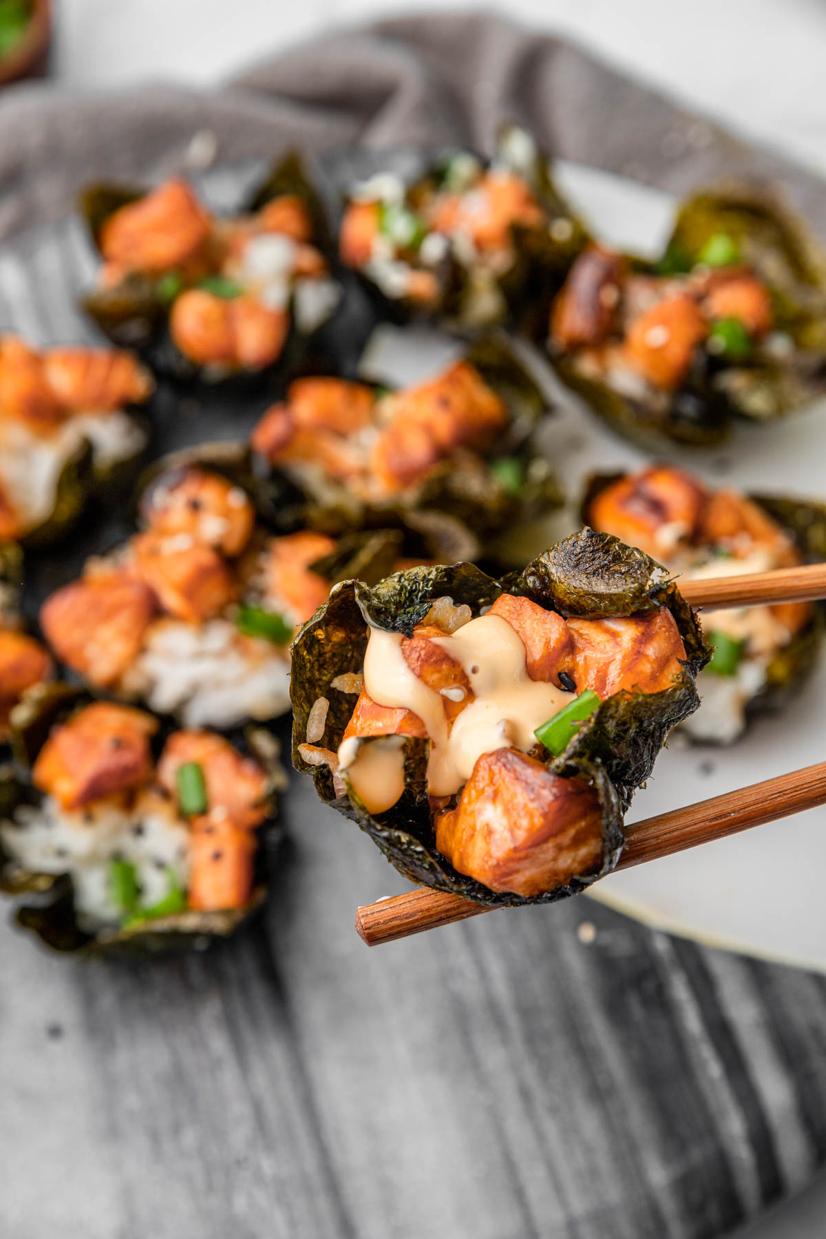 Zoomed in photo of salmon sushi in a nori cup with spicy mayonnaise and green onions.