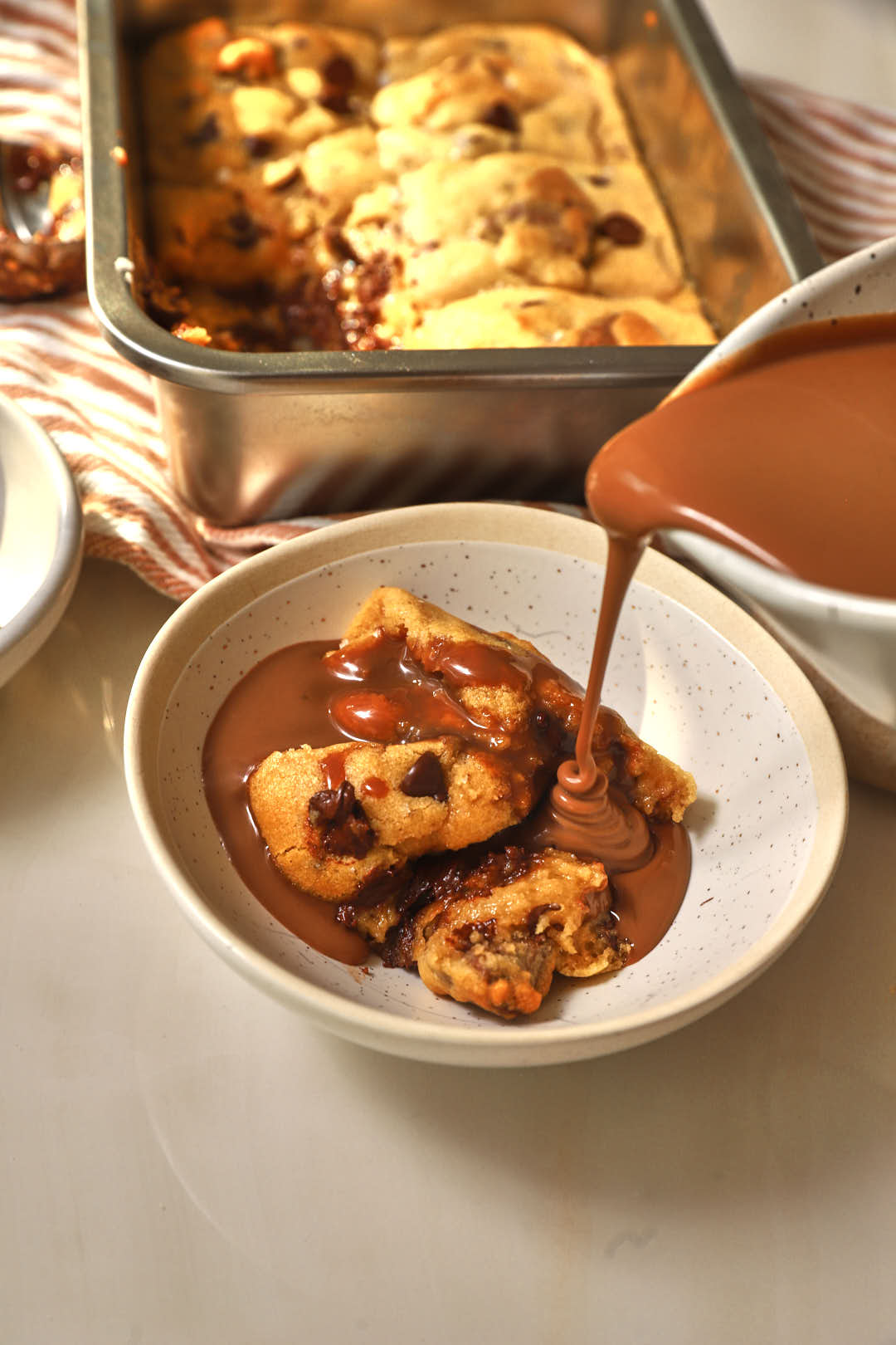 a photo of chocolate sauce being poured onto gooey deep dish chocolate chip cookies in a small bowl.
