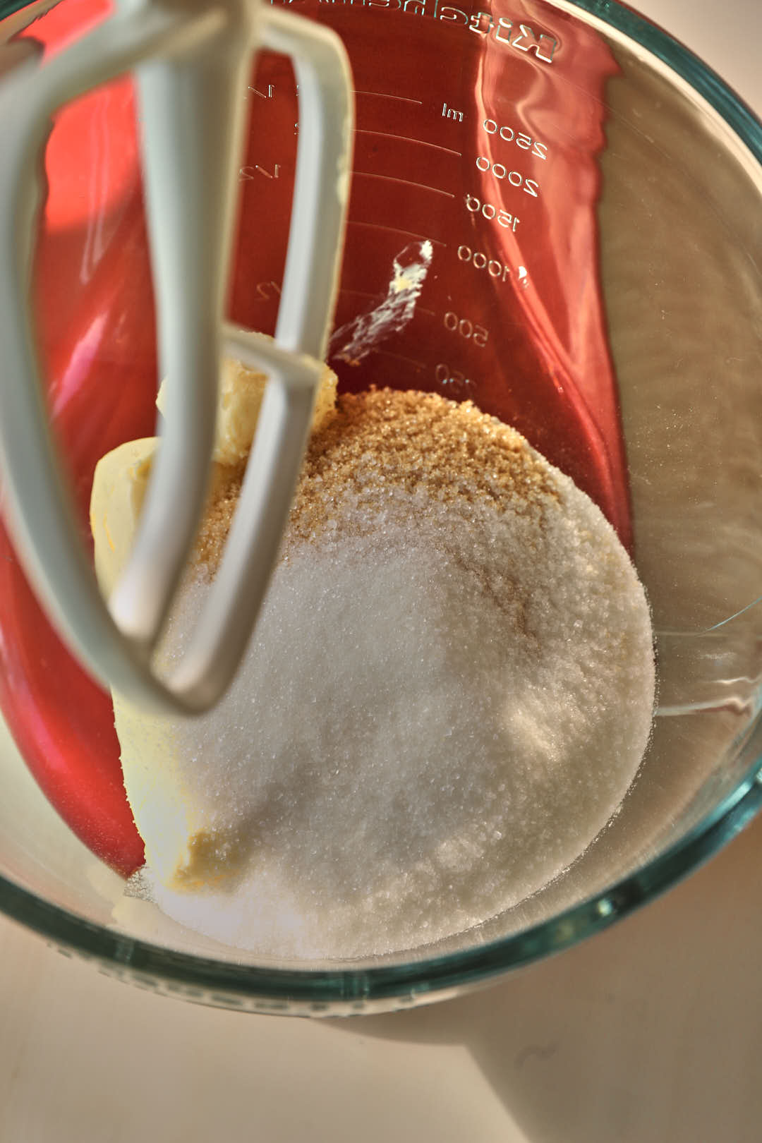 butter and brown sugar and granulated sugar added to a glass kitchen aid bowl.