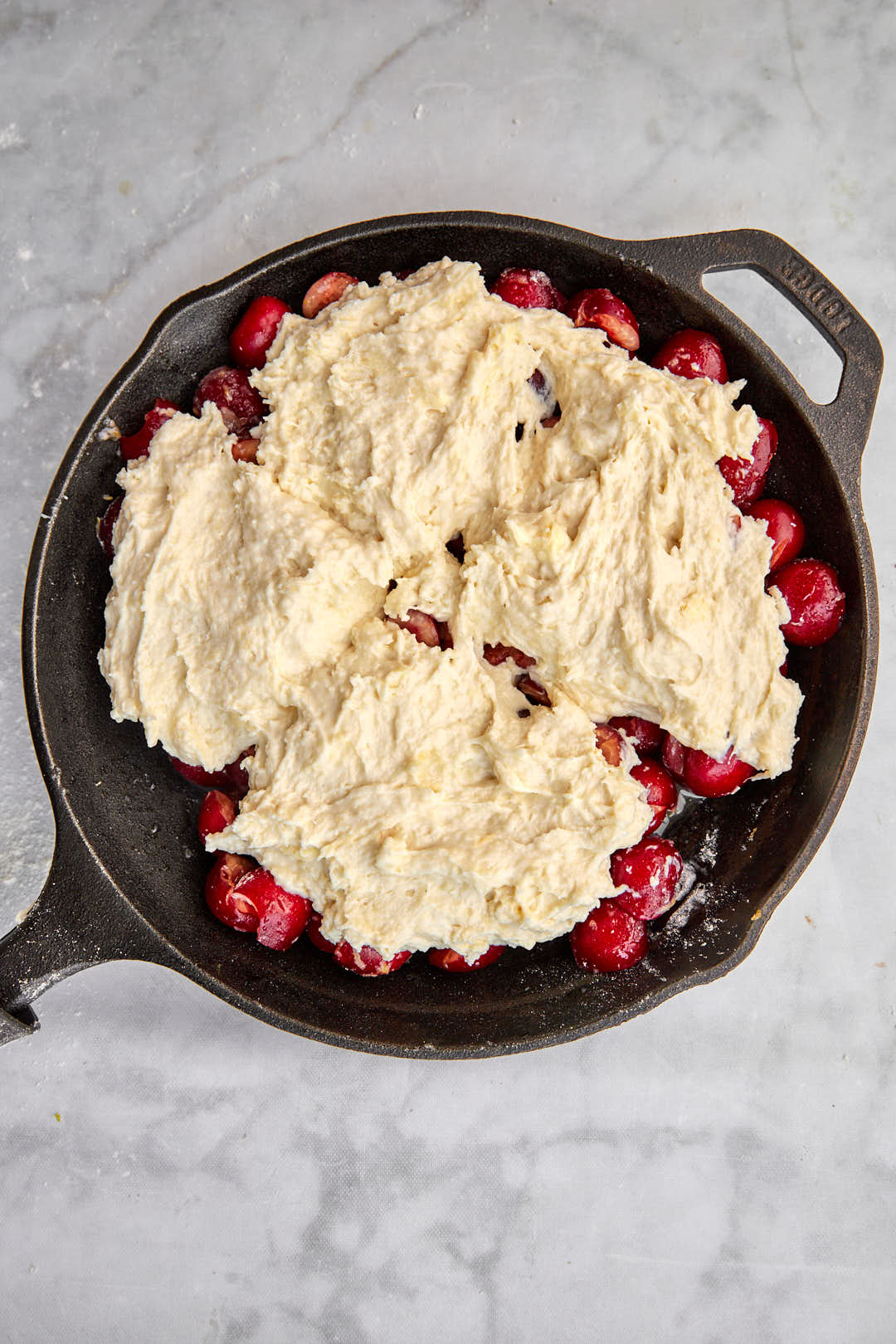 Buttermilk biscuit dough dolloped onto cherry filling in cast iron skillet.