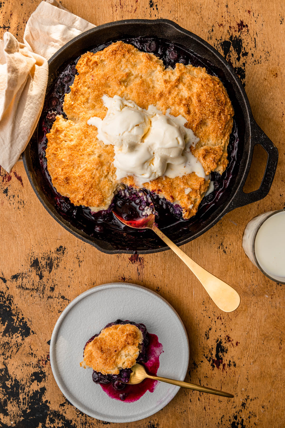 blueberry cobbler in a skillet with a glass of milk and a plate