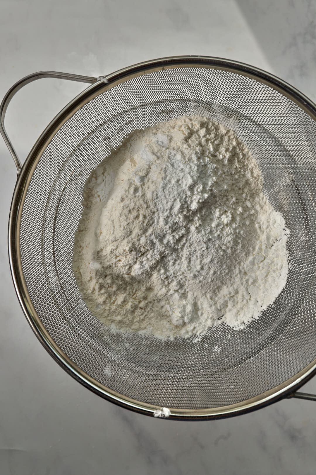 dry ingredients for cookies in a sifter over a glass bowl.