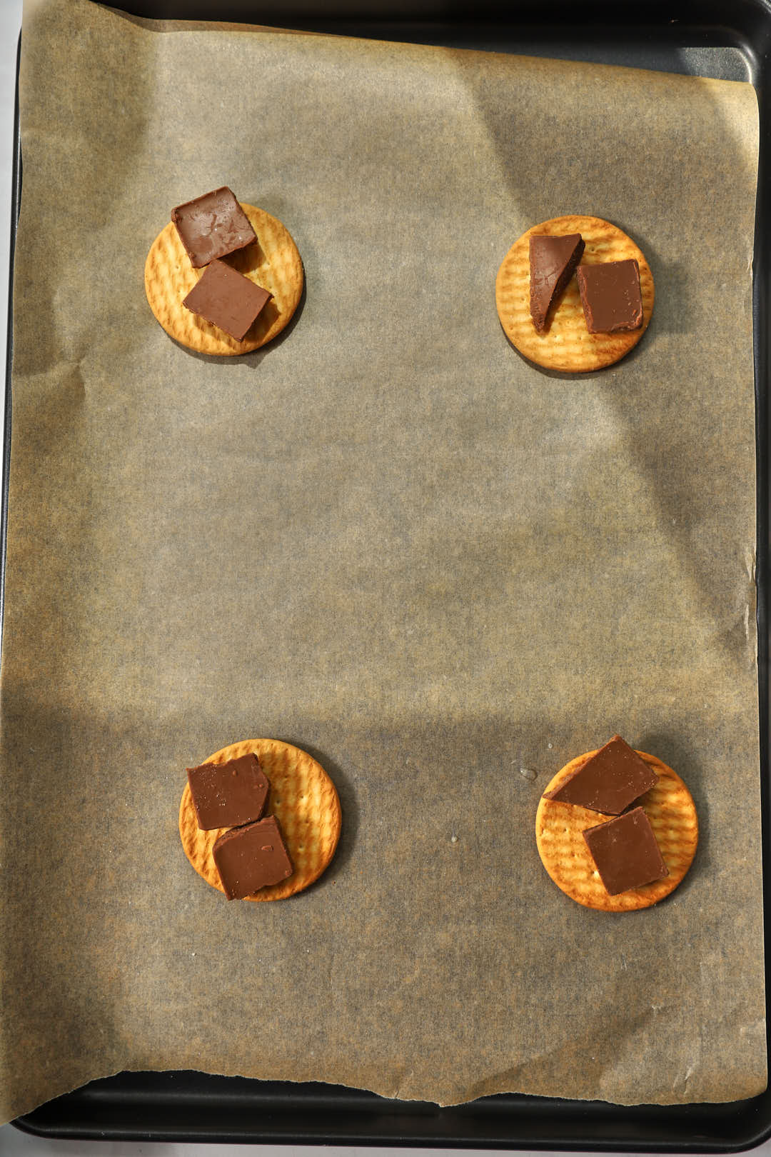 chocolate chunks added to biscuits on a parchment paper lined baking sheet.