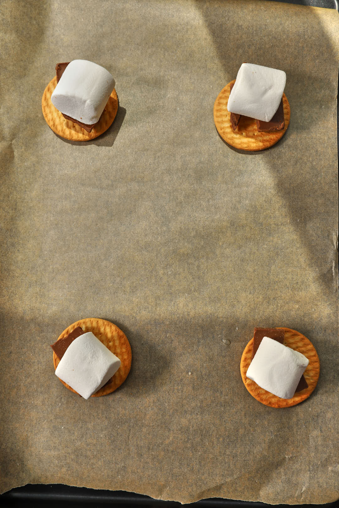 marshmallows added to chocolate chunks on a biscuit on a parchment paper lined baking sheet.