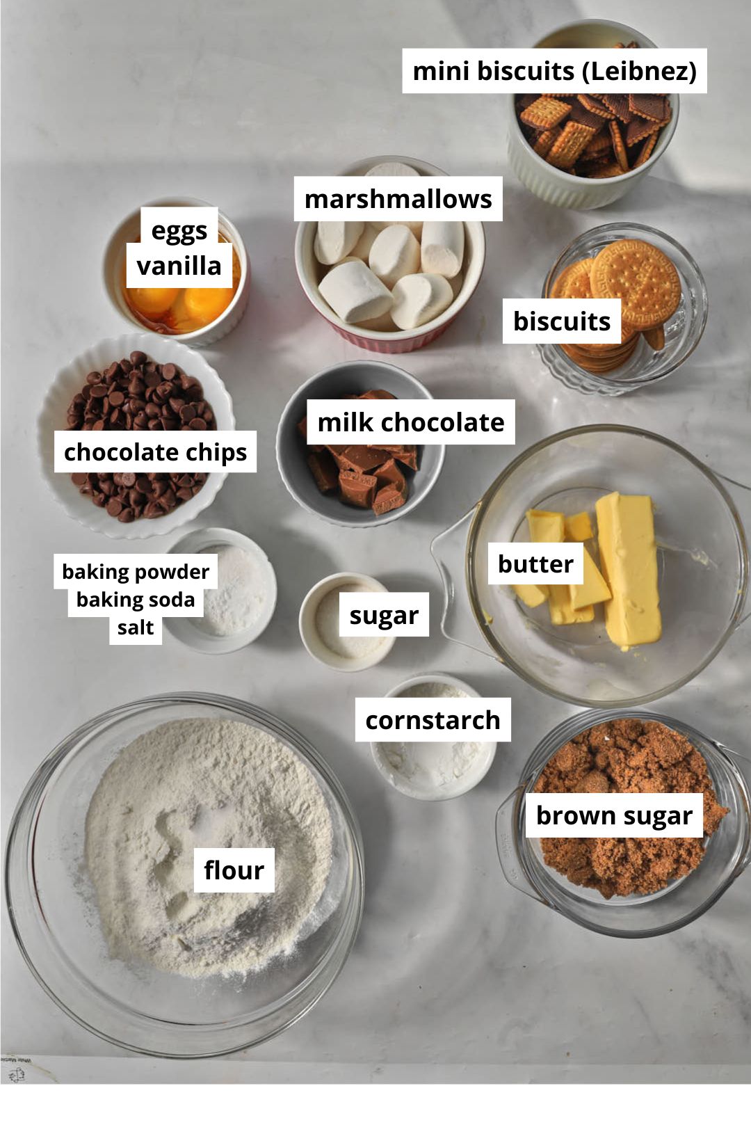 the ingredients you need to make s'mores stuffed cookies on a white marble background