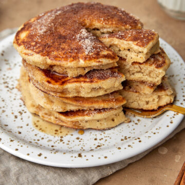 stack of snickerdoodle pacnakes on a white plate with a bite being taken out.