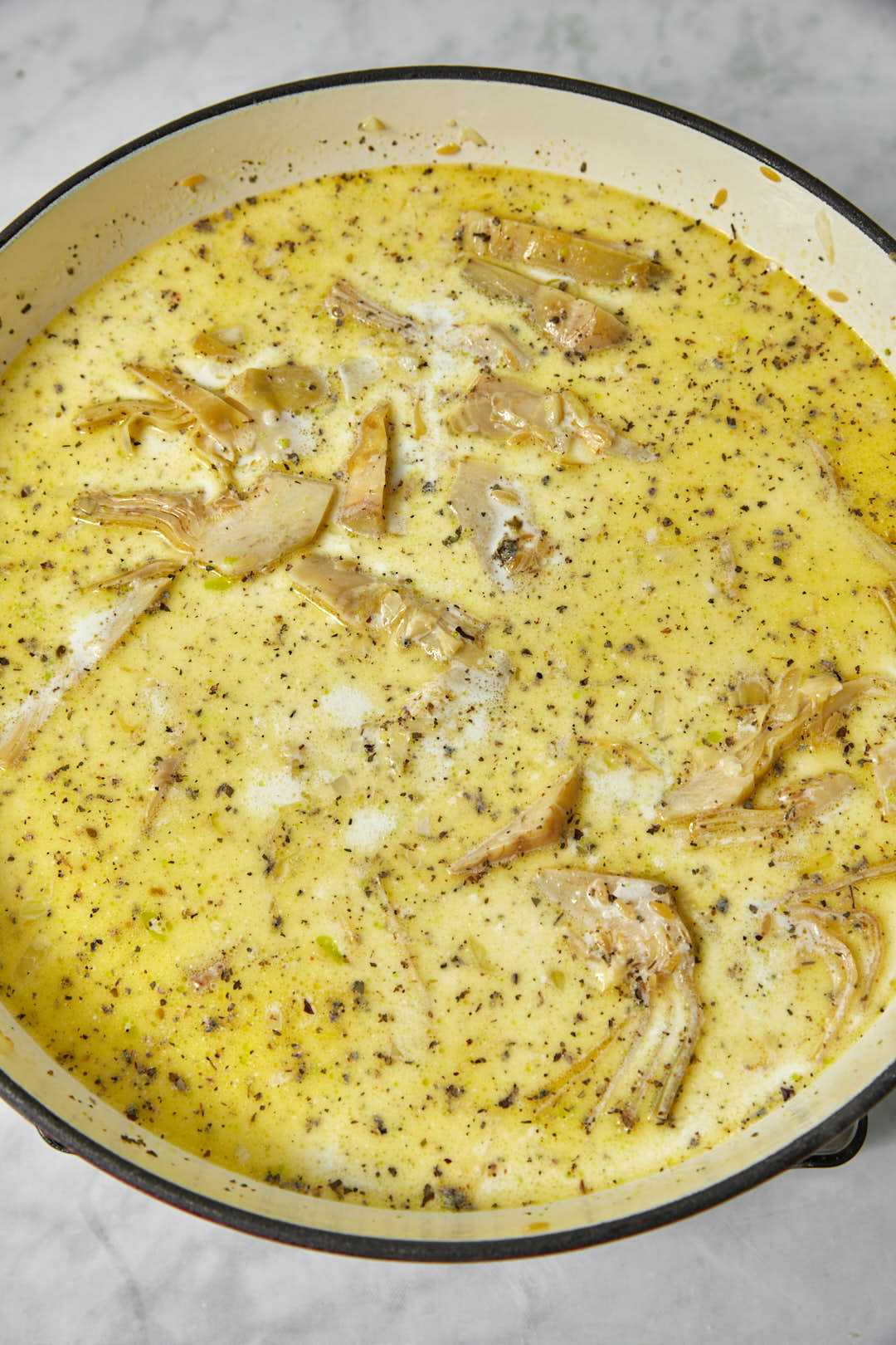 artichokes and orzo simmering in cream in a large skillet.