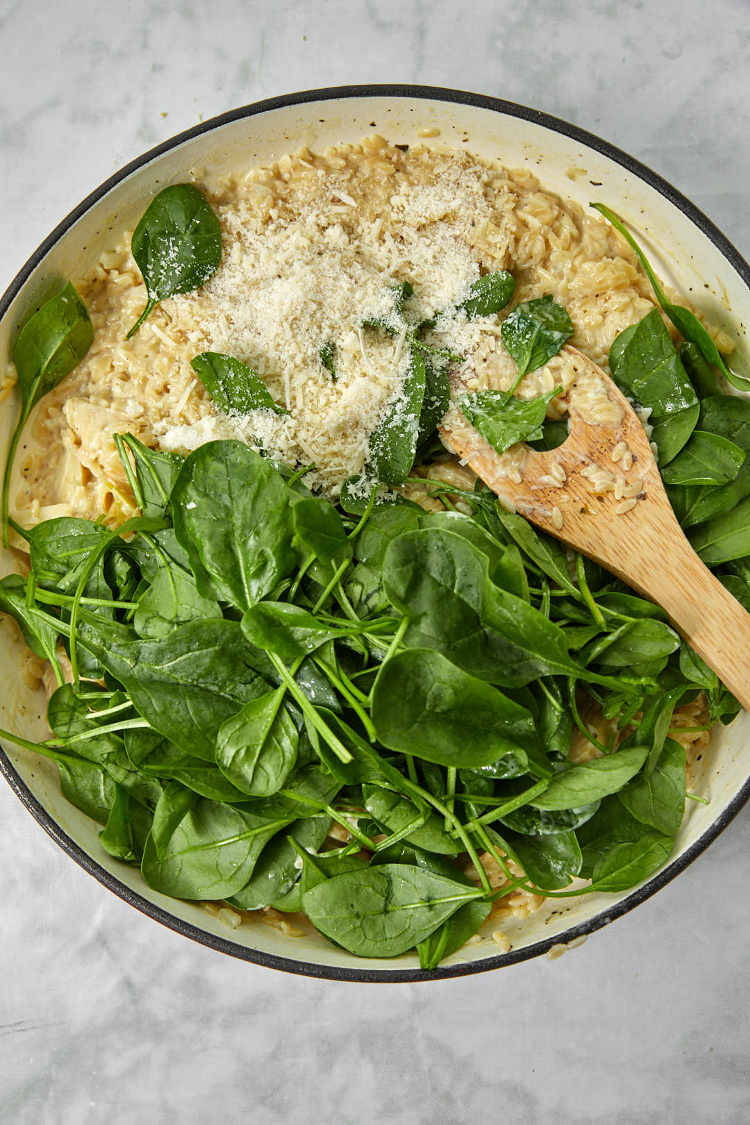 baby spinach and paremsan cheese added to orzo in a large skillet.