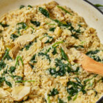 Creamy spinach artichoke orzo with a wooden spoon in the saucepan.