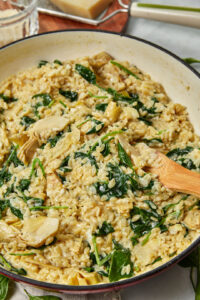 Creamy spinach artichoke orzo with a wooden spoon in the saucepan.