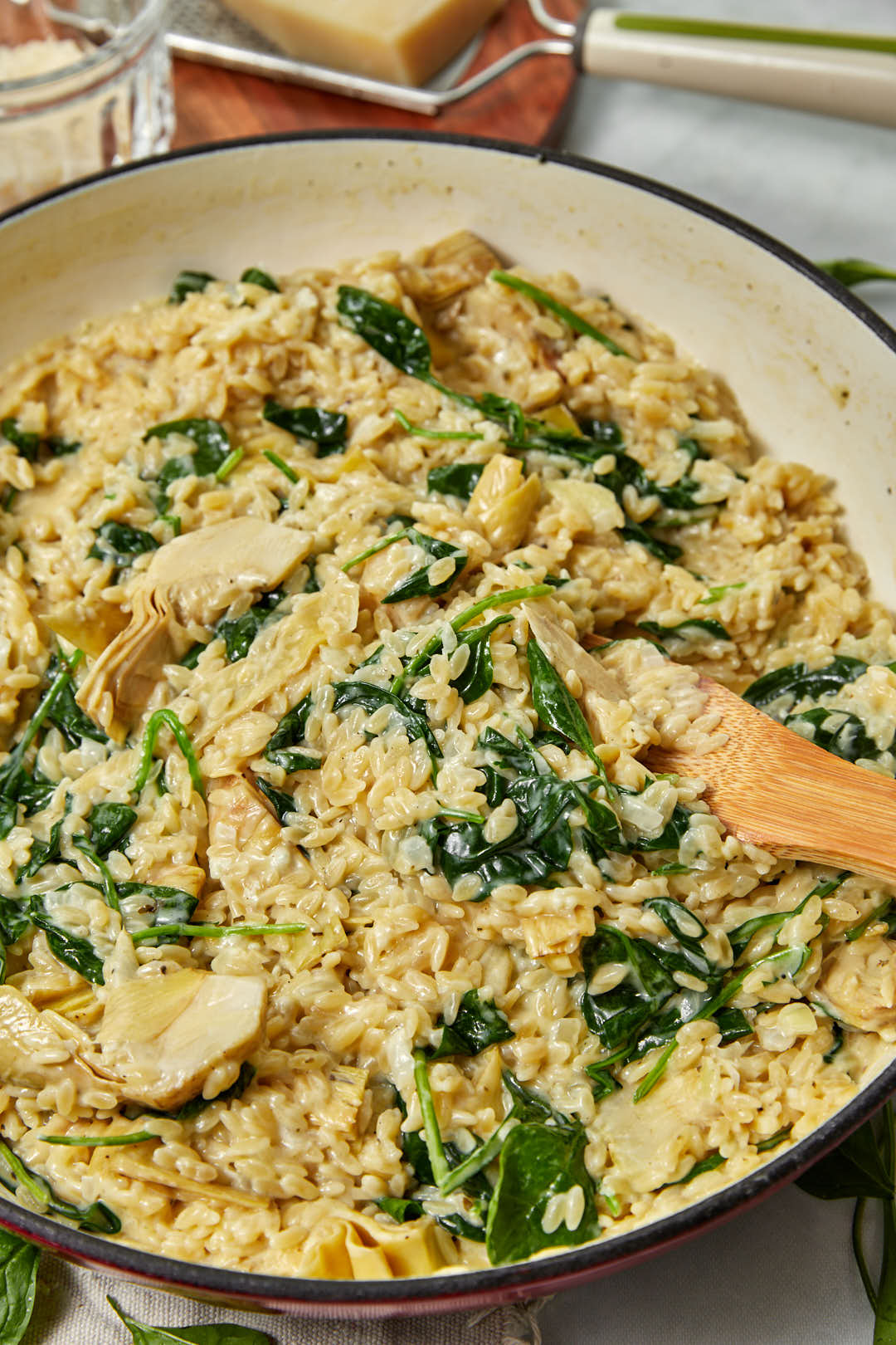 Creamy spinach artichoke orzo with a wooden spoon in the saucepan.