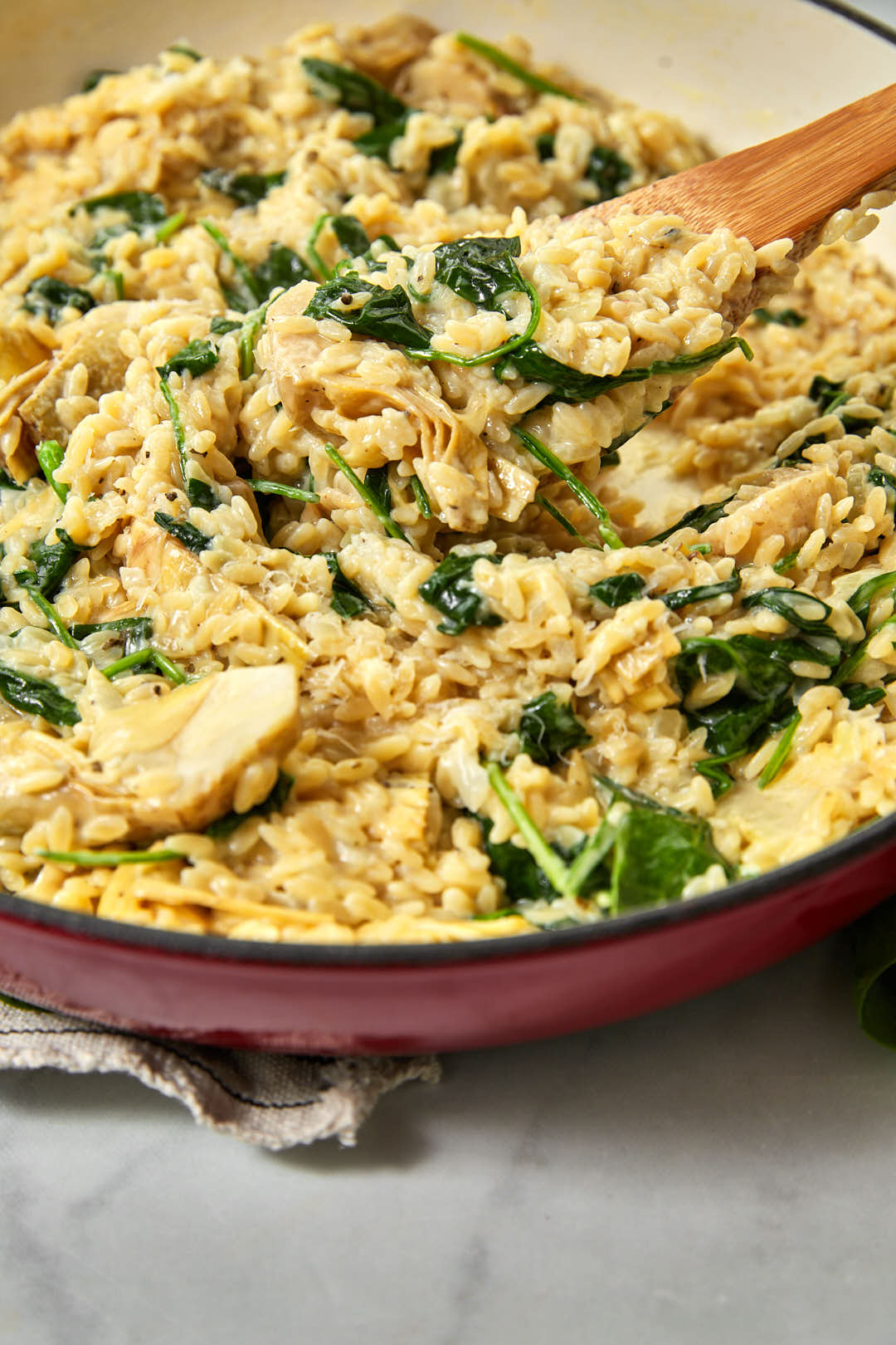 a wooden spoon scooping some spinach orzo out of a saucepan.