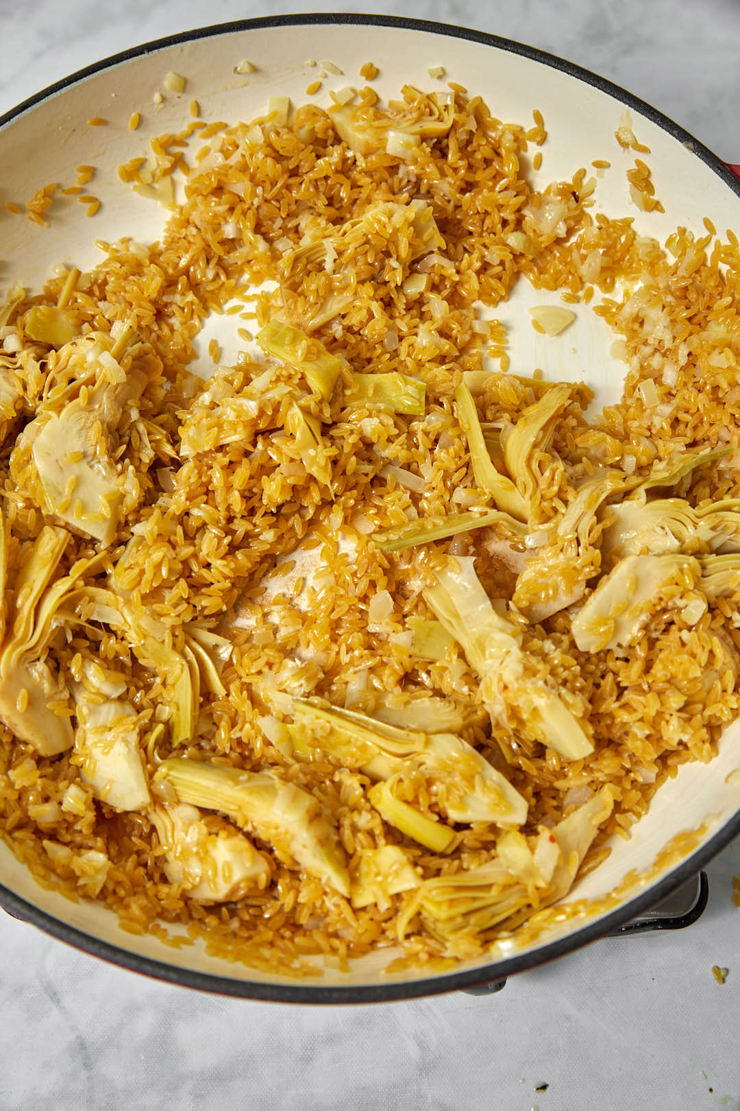 orzo being toasted in a large skillet with artichoke.