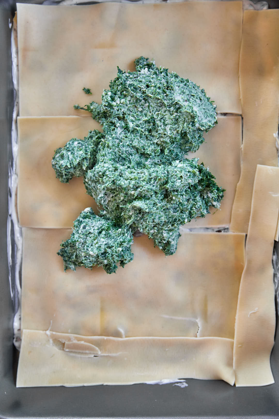 spinach ricotta filling being dolloped onto lasagna noodles.