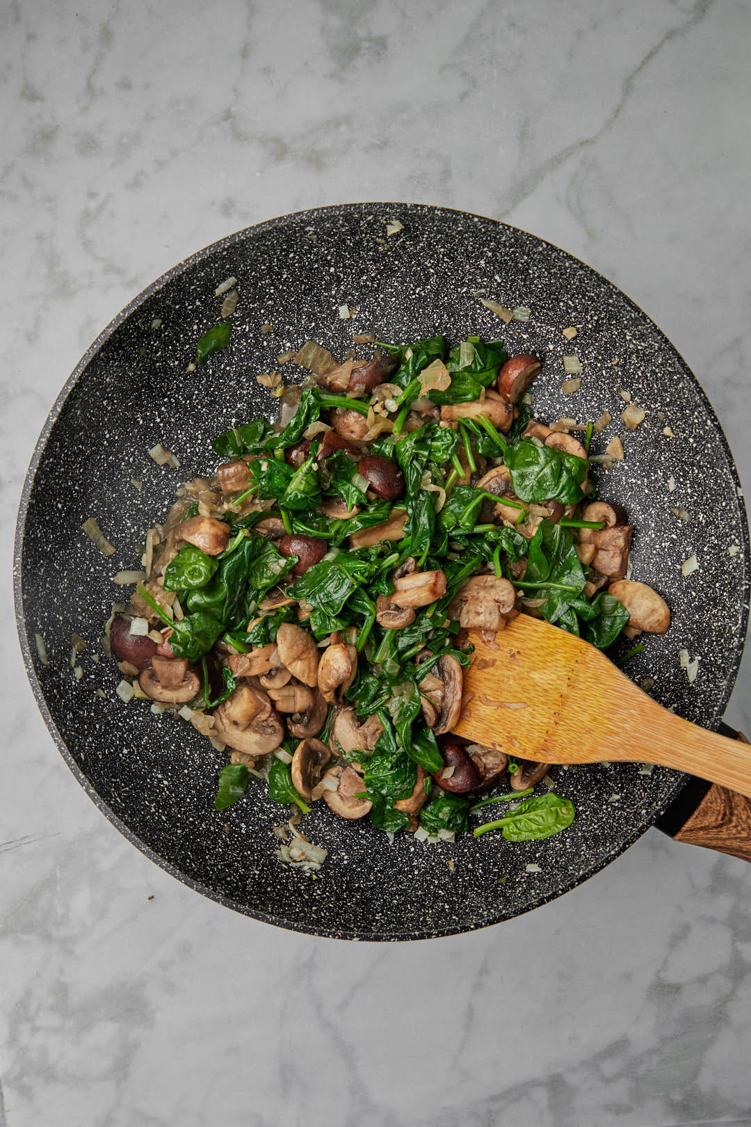 spinach wilted in a skillet with mushrooms and onions.