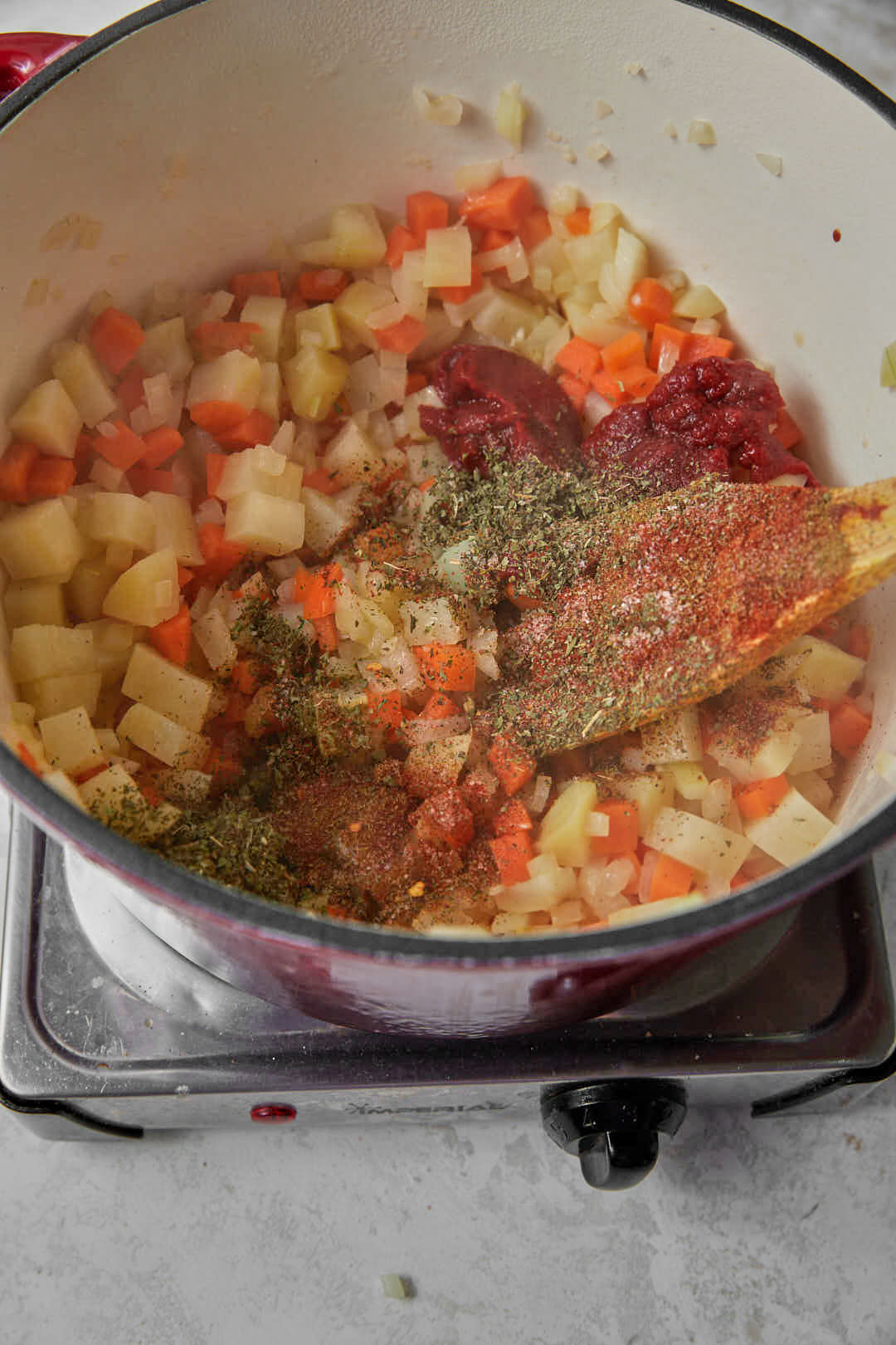Tomato paste and spices added to diced onions, carrots and onions in saucepan.
