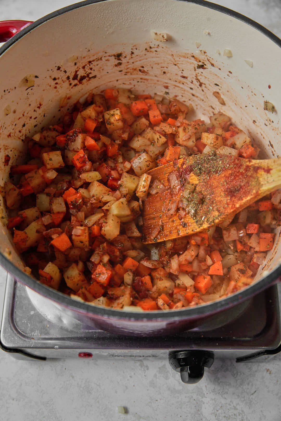 tomato paste stirred through chopped vegetables in a saucepan.