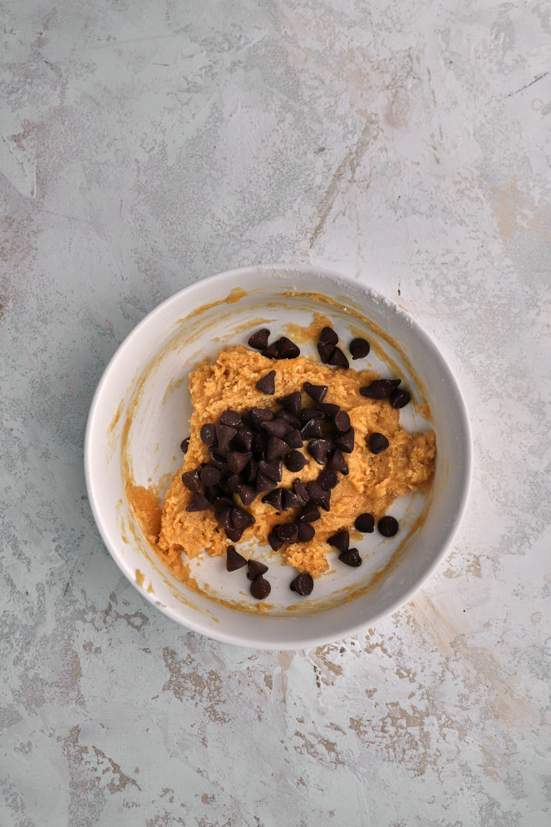 Chocolate chips added to cookie dough in small bowl.