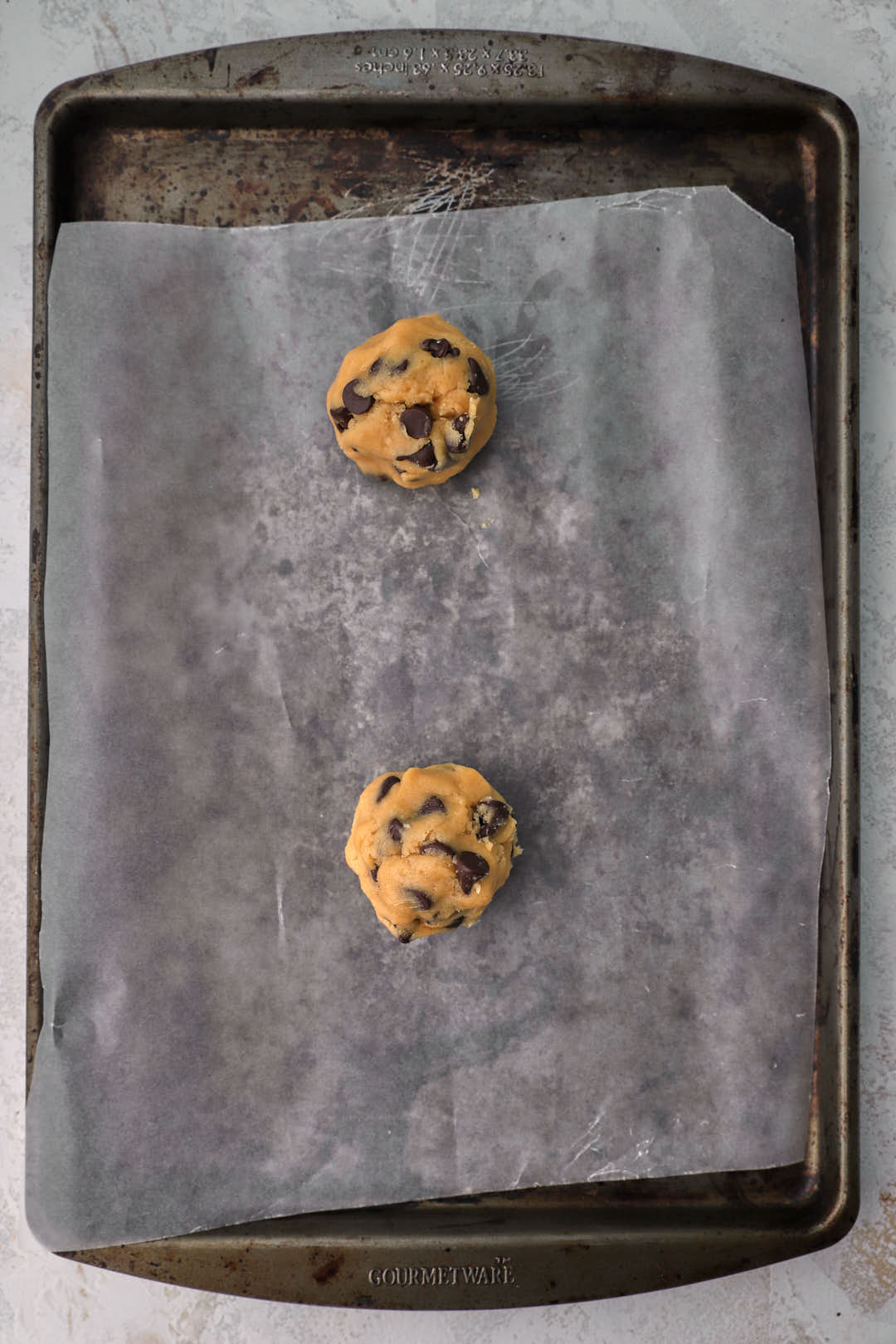 two cookie dough balls on parchment paper lined baking sheet.