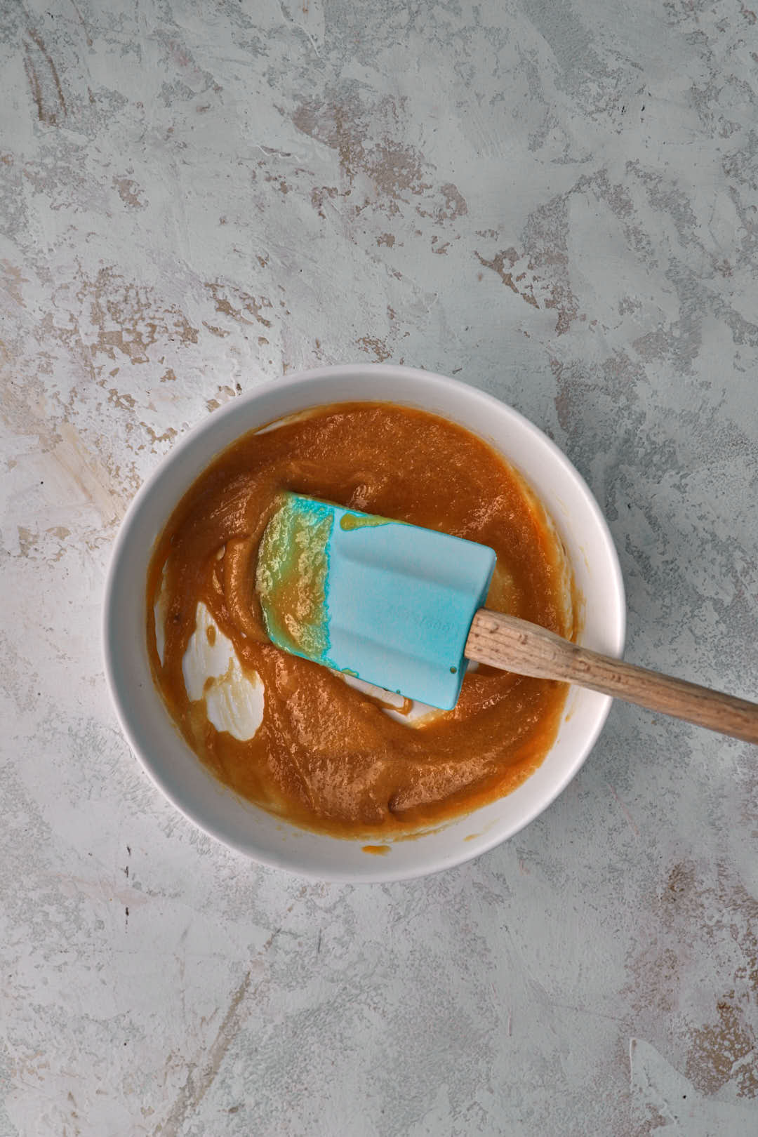 cookie dough being stirred in small white bowl with a blue spatula.