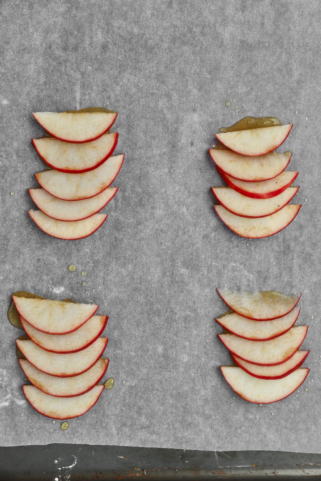 Thin apple slices spaced apart on parchment paper lined baking sheet.