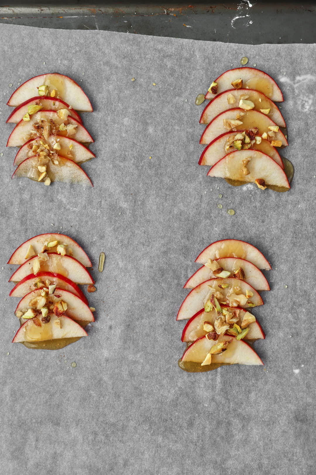 chopped pistachio nuts on apple slices on a baking sheet.