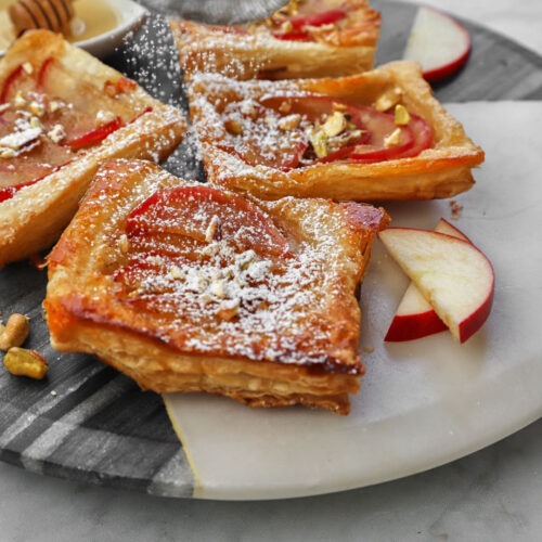 icing sugar being sifted onto apple puff pastry square on a marble cake board.