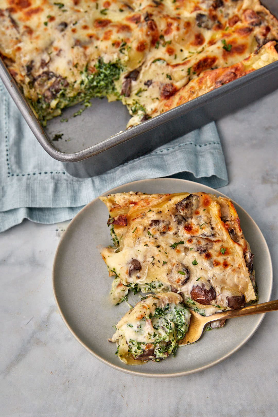 a fork taking a bite out of the spinach bechamel lasagna on a gray plate.
