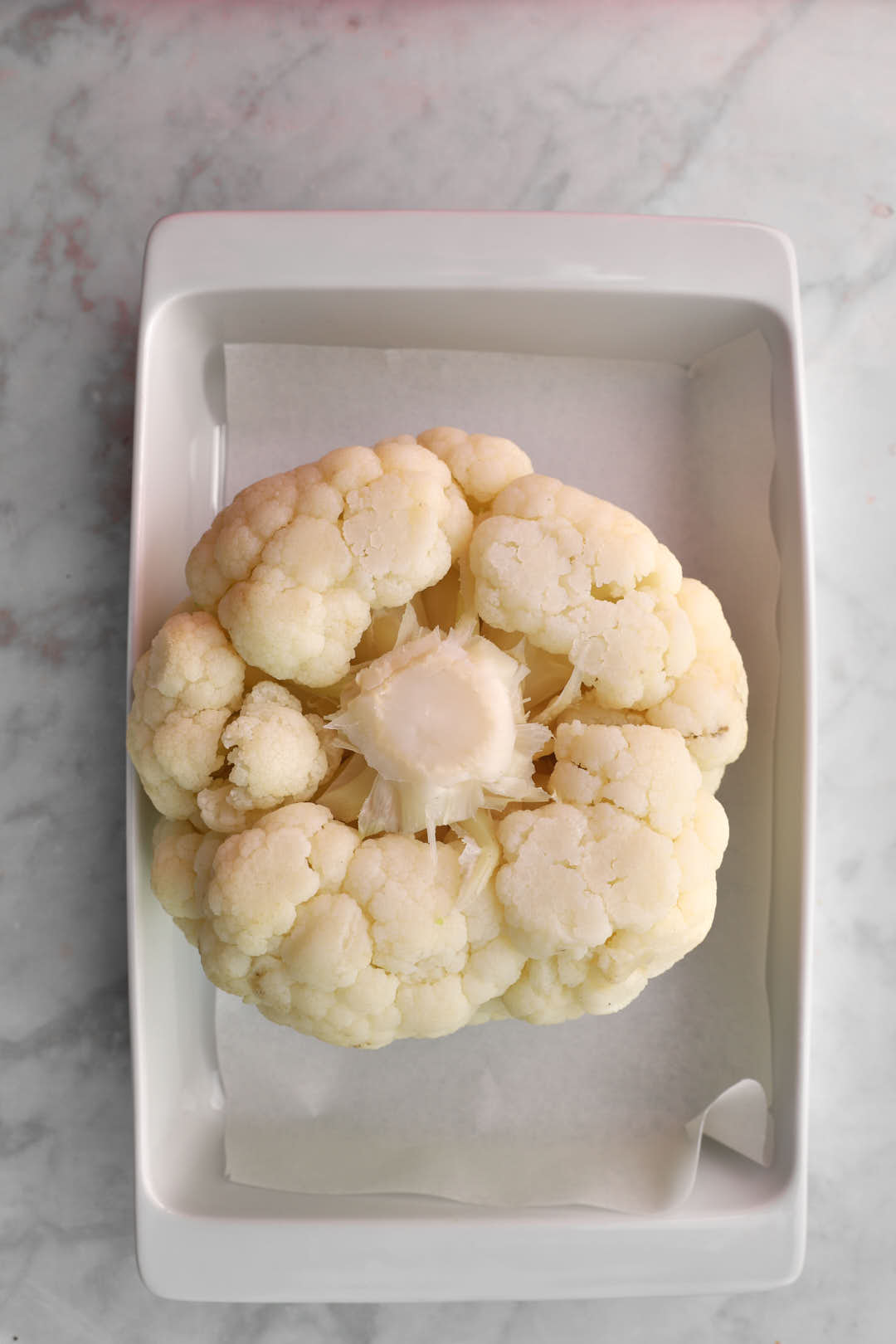 drained and dried whole roasted cauliflower in a white baking pan.