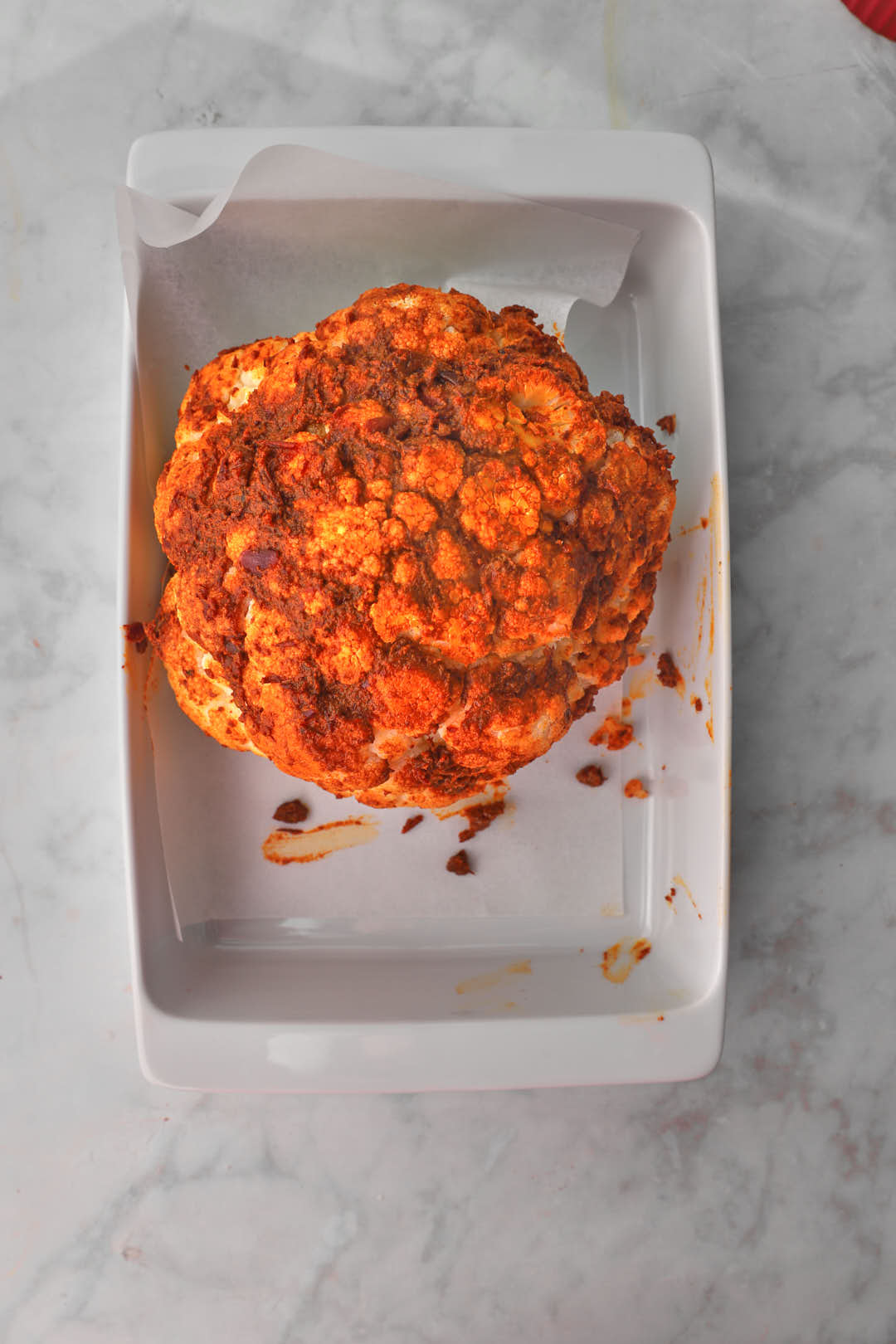 Whole cauliflower in baking pan rubbed all over with red pepper and spice paste.