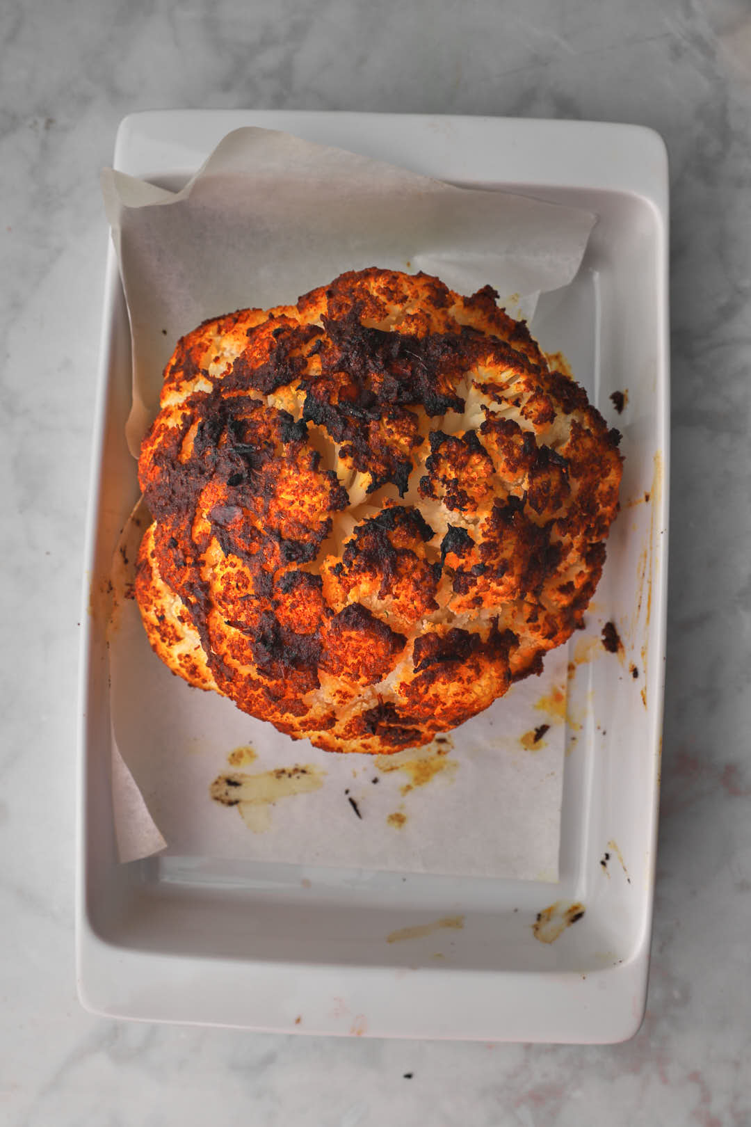 Roasted whole cauliflower in a white baking pan.