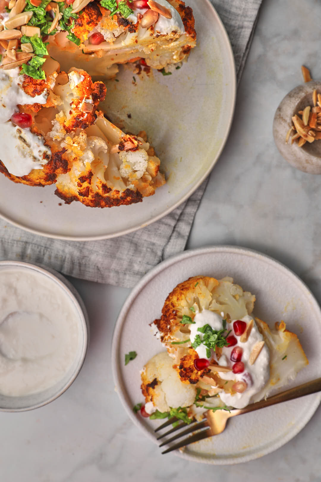 sliced whole roasted cauliflower with tahini sauce on the side in two plates.